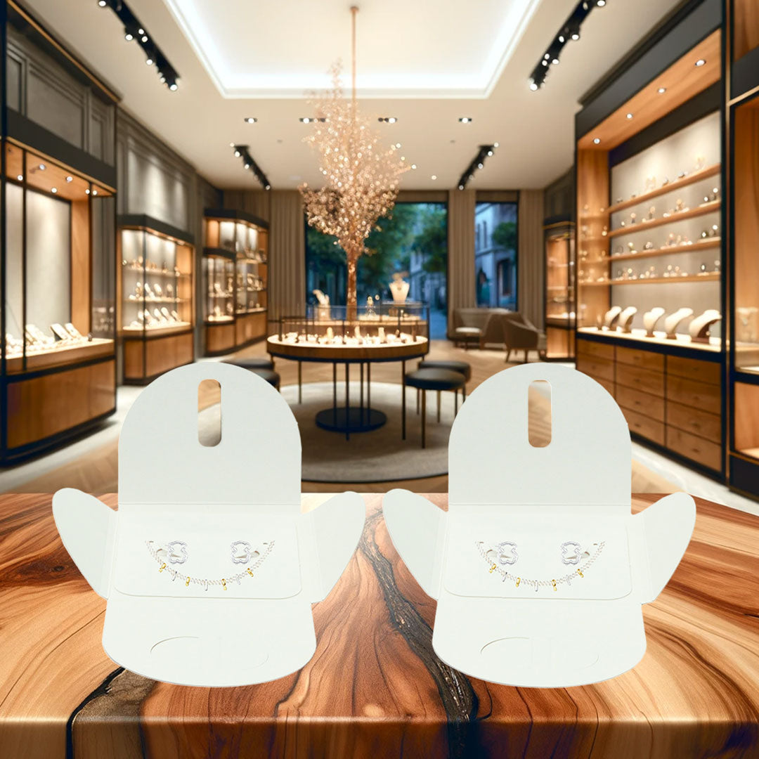 La imagen muestra dos elegantes cajitas blancas biodegradables, exhibiendo unos collares y aretes de manera muy elegante en el mostrador de una joyería.